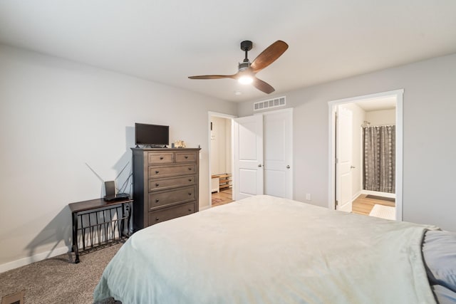 carpeted bedroom with a ceiling fan, visible vents, ensuite bath, and baseboards