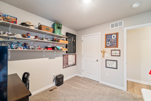 carpeted office with a textured ceiling, visible vents, and baseboards