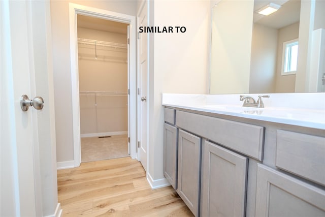 bathroom with a spacious closet, baseboards, wood finished floors, and vanity