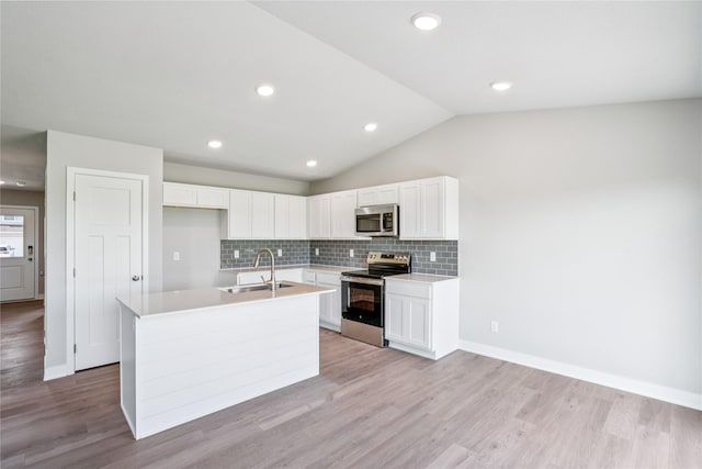 25091 Bluebird Cir, Adel, IA 50003 - kitchen featuring appliances with stainless steel finishes, an island with sink, backsplash, vaulted ceiling, and white cabinets