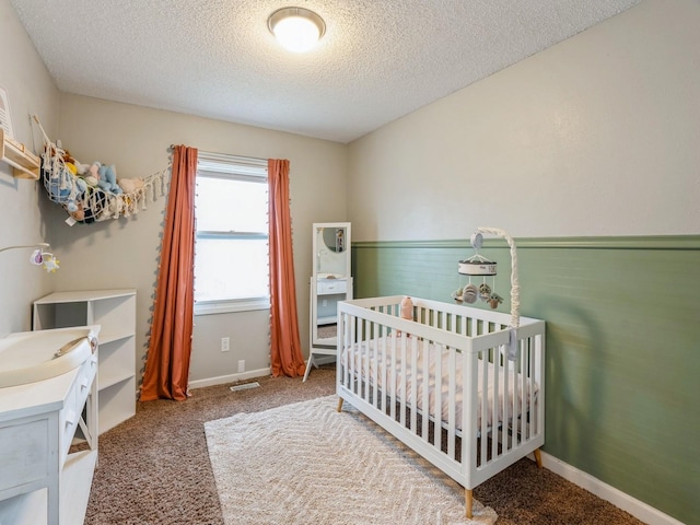 bedroom with a crib, baseboards, a textured ceiling, and carpet flooring