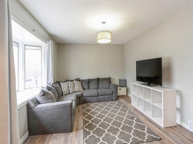 living area featuring baseboards, a textured ceiling, visible vents, and wood finished floors