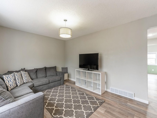 living room featuring baseboards, a textured ceiling, visible vents, and wood finished floors