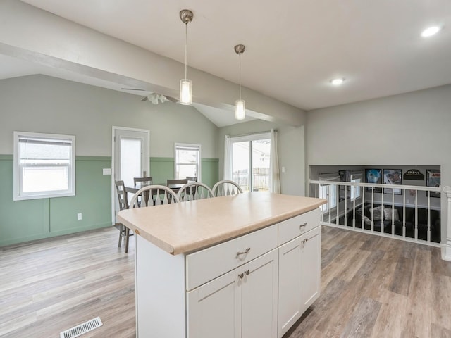 kitchen with visible vents, white cabinets, vaulted ceiling, light wood finished floors, and decorative light fixtures