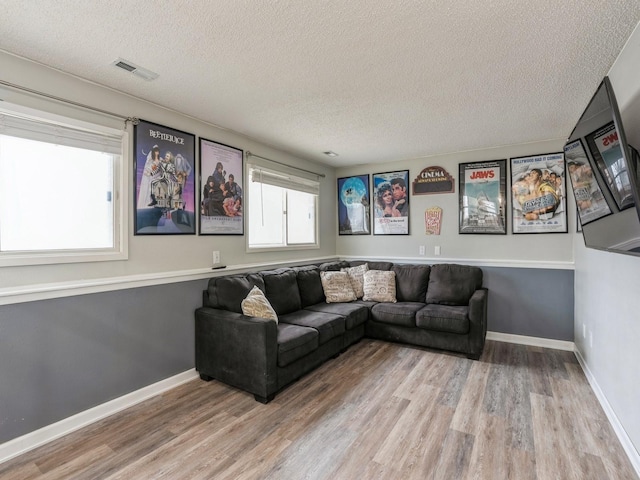 living room with baseboards, a textured ceiling, visible vents, and wood finished floors