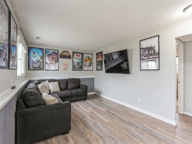 living area with light wood-style flooring, baseboards, and a textured ceiling