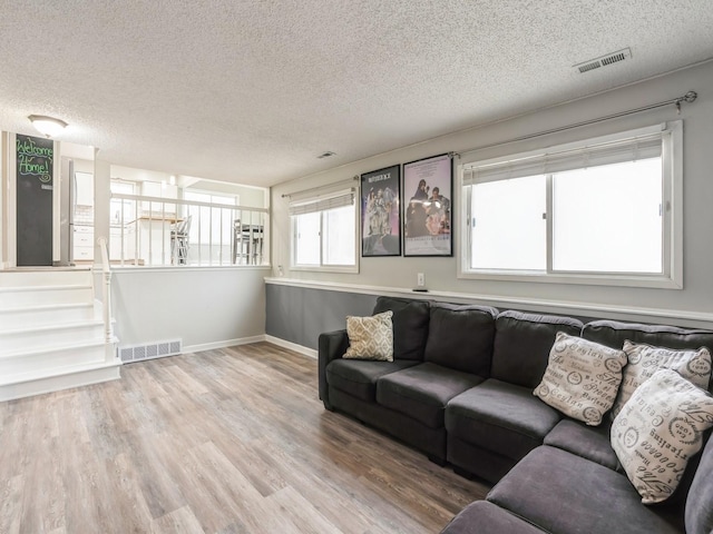 living area with baseboards, a textured ceiling, visible vents, and wood finished floors