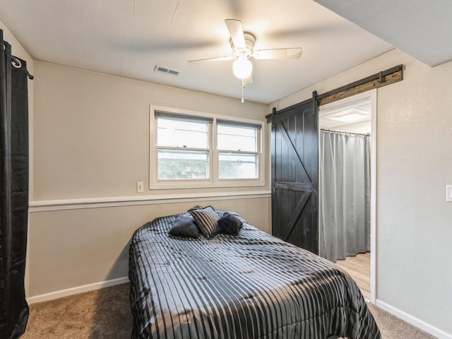 bedroom featuring a barn door, visible vents, baseboards, and carpet flooring