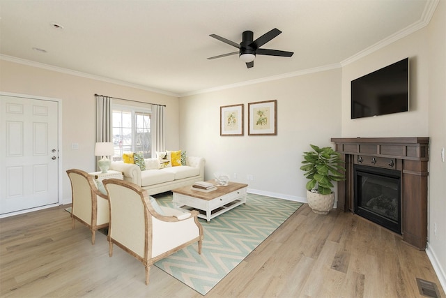 living room featuring visible vents, a ceiling fan, crown molding, wood finished floors, and a glass covered fireplace