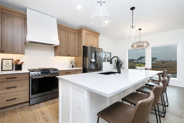 kitchen featuring a sink, light countertops, appliances with stainless steel finishes, a kitchen bar, and custom range hood