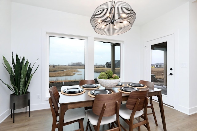 dining room featuring a water view, light wood-style flooring, baseboards, and an inviting chandelier