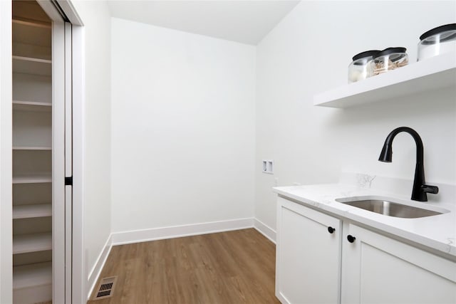 laundry room featuring hookup for a washing machine, light wood-style flooring, a sink, visible vents, and cabinet space