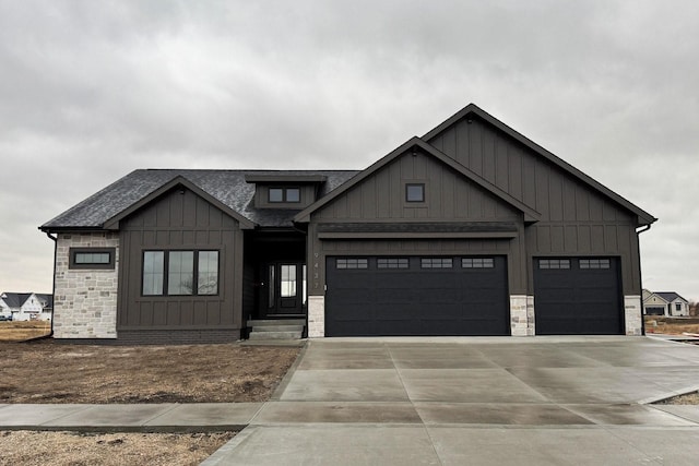 view of front of house featuring driveway, roof with shingles, stone siding, a garage, and board and batten siding