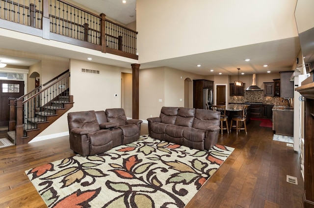 living room featuring arched walkways, dark wood-style flooring, visible vents, and stairs