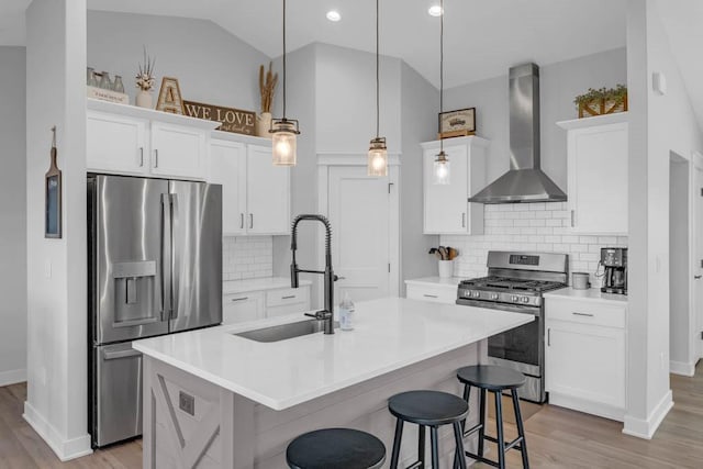 kitchen with a center island with sink, light countertops, appliances with stainless steel finishes, a sink, and wall chimney range hood