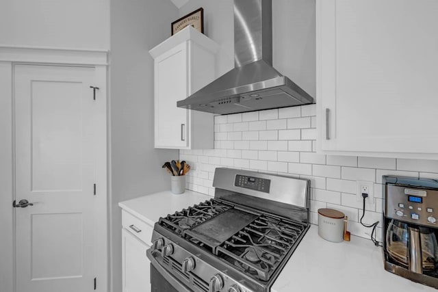 kitchen with stainless steel gas stove, white cabinets, decorative backsplash, wall chimney exhaust hood, and light countertops