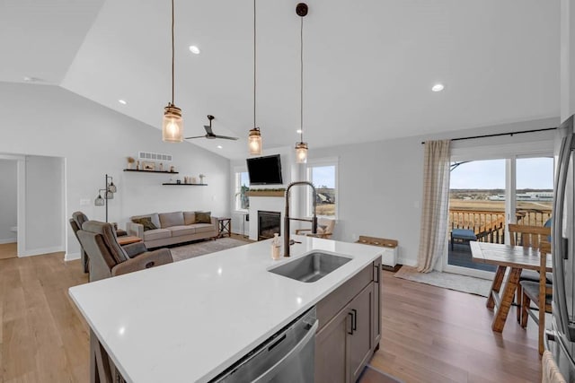 kitchen featuring light wood-style floors, a glass covered fireplace, vaulted ceiling, a sink, and dishwasher