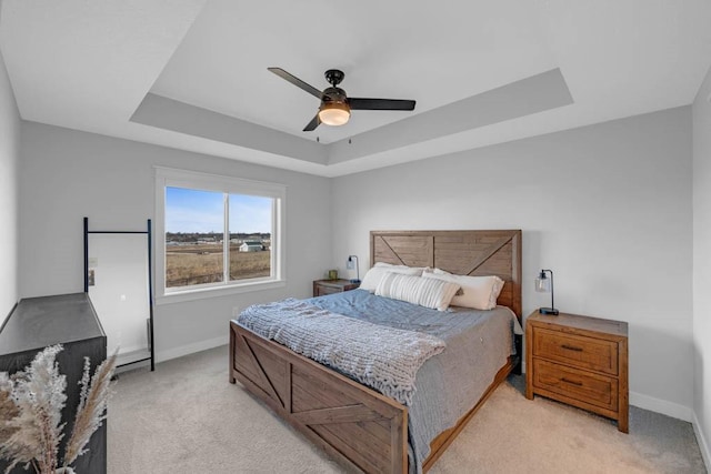 bedroom featuring light carpet, baseboards, a tray ceiling, and ceiling fan