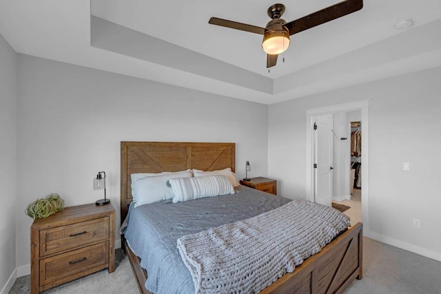 bedroom with a ceiling fan, a tray ceiling, light carpet, and baseboards