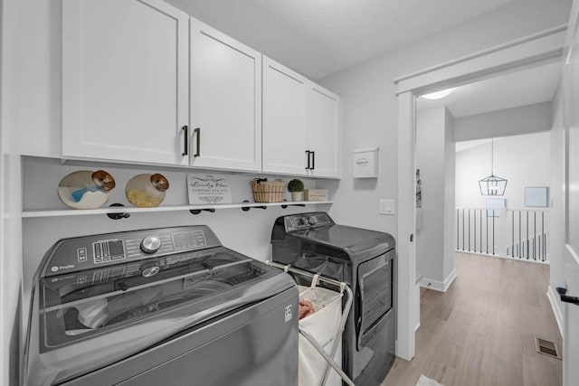 washroom featuring light wood-type flooring, cabinet space, washing machine and dryer, and visible vents