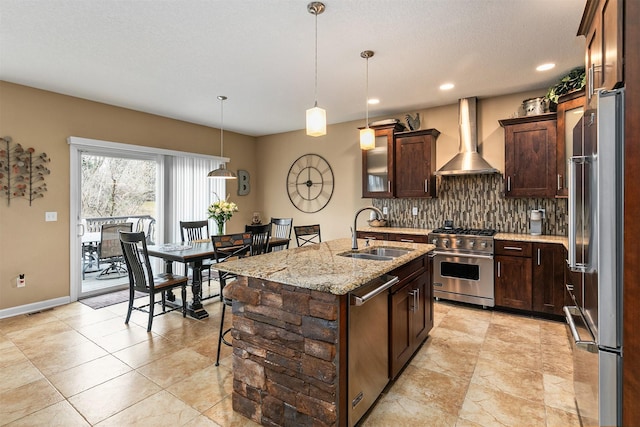 kitchen featuring dark brown cabinetry, premium appliances, wall chimney exhaust hood, backsplash, and a sink