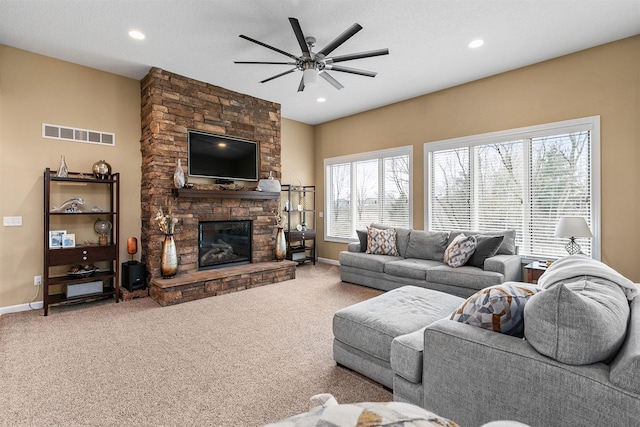 living room featuring carpet floors, a stone fireplace, visible vents, and baseboards