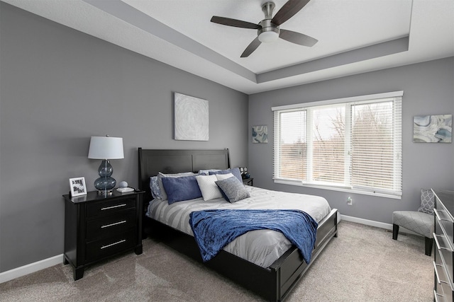 carpeted bedroom with a ceiling fan, a tray ceiling, and baseboards