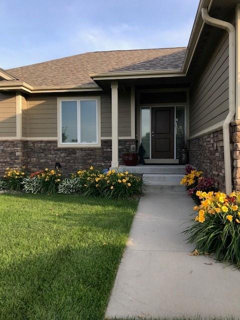 entrance to property featuring stone siding, a lawn, and roof with shingles