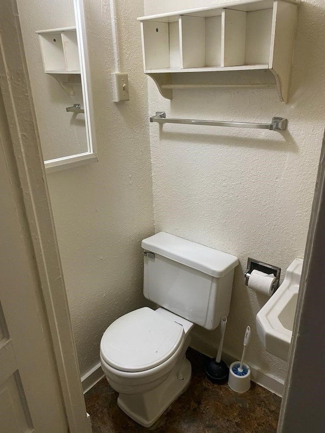 bathroom with baseboards, a textured wall, and toilet