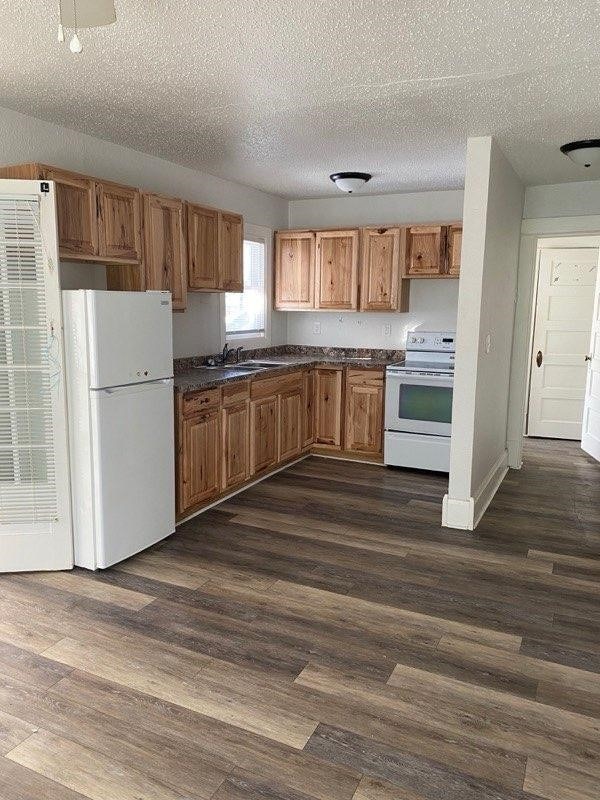 kitchen with a textured ceiling, white appliances, dark countertops, and dark wood finished floors