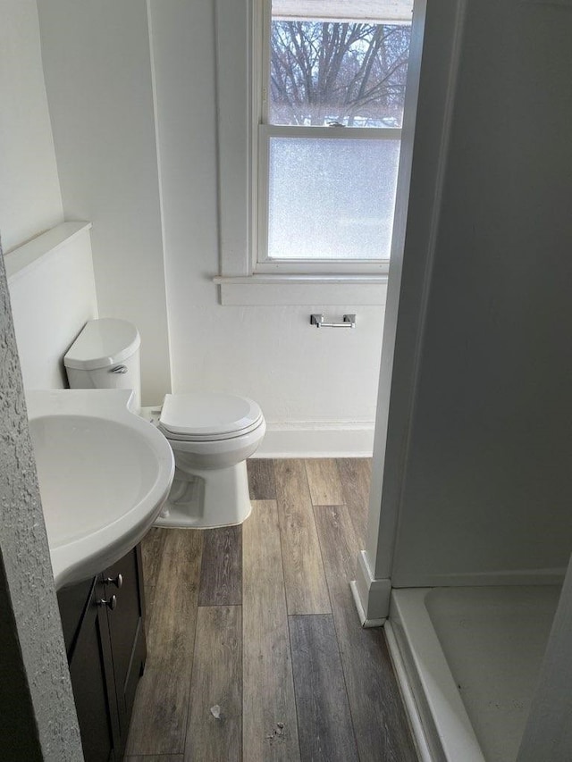 full bathroom featuring a stall shower, baseboards, toilet, wood finished floors, and a sink