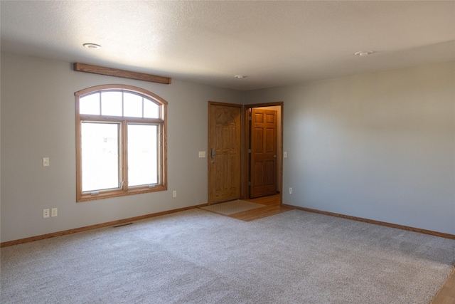 empty room with light carpet, visible vents, baseboards, and a textured ceiling