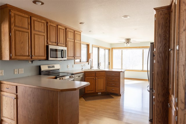 kitchen with a ceiling fan, a peninsula, stainless steel appliances, light wood-style floors, and a sink