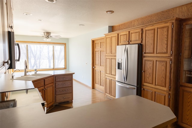 kitchen featuring stainless steel fridge with ice dispenser, brown cabinets, a peninsula, light wood-type flooring, and a sink