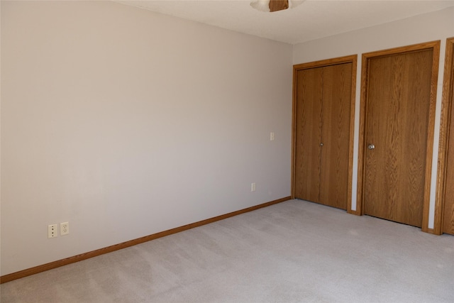 unfurnished bedroom featuring baseboards, light colored carpet, and multiple closets