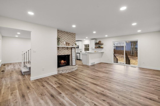 unfurnished living room featuring a fireplace, stairway, light wood-style flooring, and recessed lighting