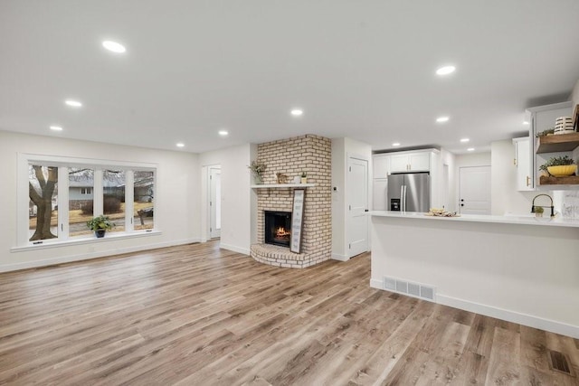 unfurnished living room featuring a fireplace, light wood-type flooring, visible vents, and a sink