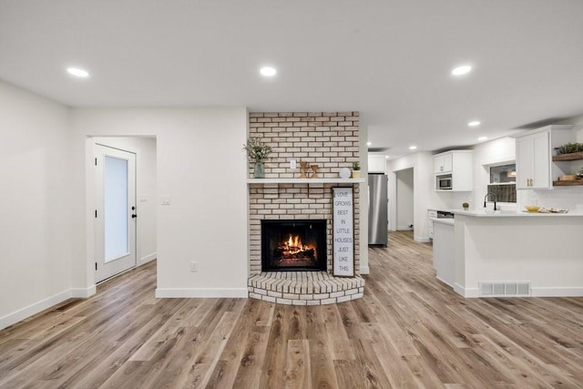 unfurnished living room featuring recessed lighting, light wood-style floors, visible vents, and a brick fireplace