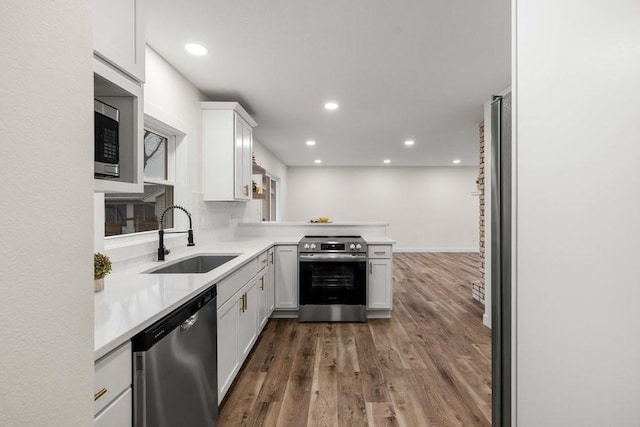 kitchen featuring a sink, light countertops, white cabinets, a peninsula, and appliances with stainless steel finishes
