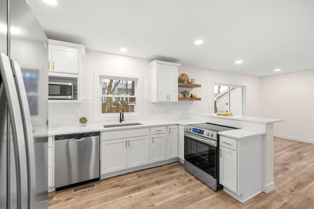 kitchen featuring stainless steel appliances, light countertops, a sink, a peninsula, and white cabinetry