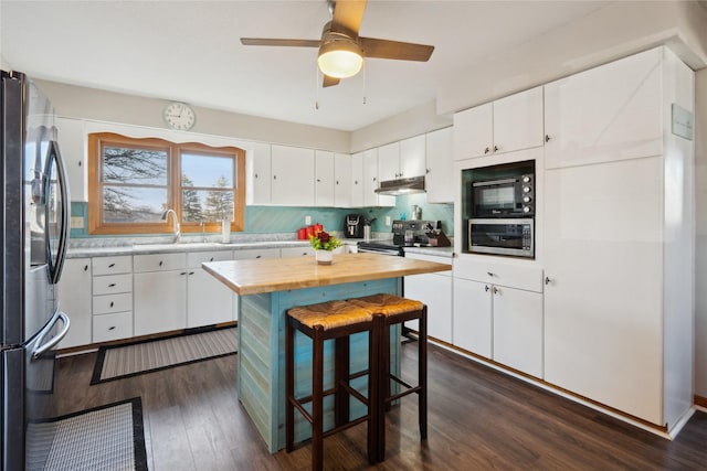 kitchen featuring butcher block countertops, dark wood-style flooring, stainless steel appliances, white cabinetry, and a sink