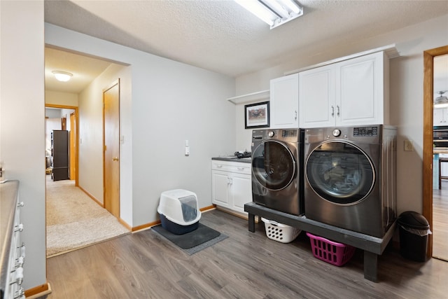 washroom with cabinet space, a textured ceiling, separate washer and dryer, wood finished floors, and baseboards