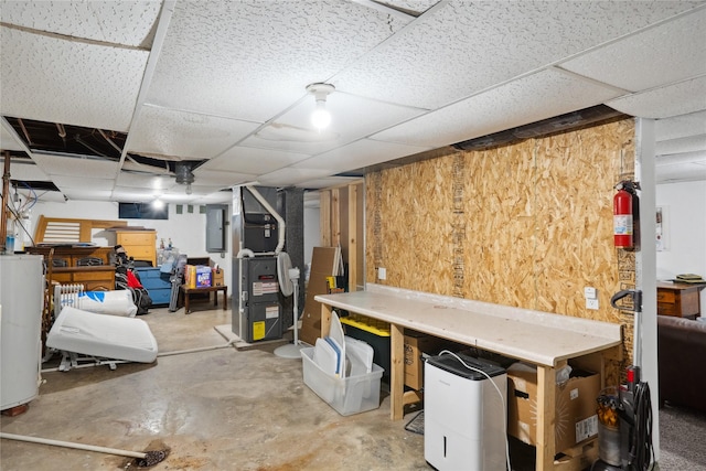 finished below grade area featuring water heater, wooden walls, a paneled ceiling, and electric panel