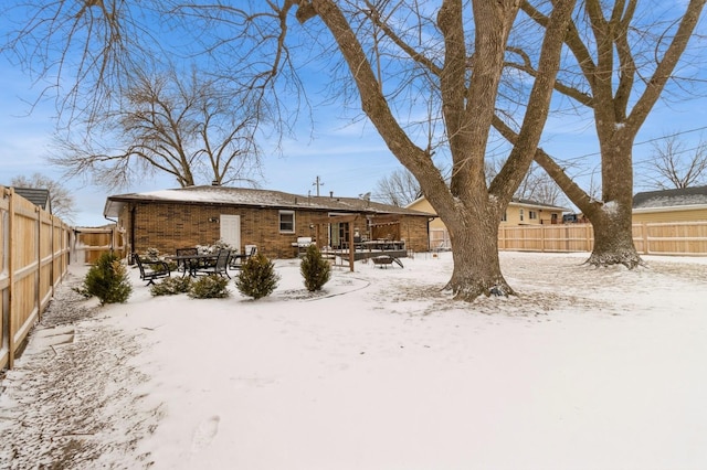 snow covered house with brick siding, a patio, and a fenced backyard