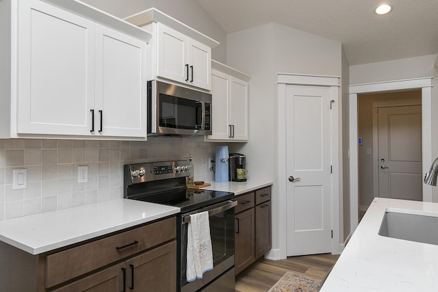 kitchen featuring appliances with stainless steel finishes, backsplash, light wood-style floors, white cabinetry, and a sink