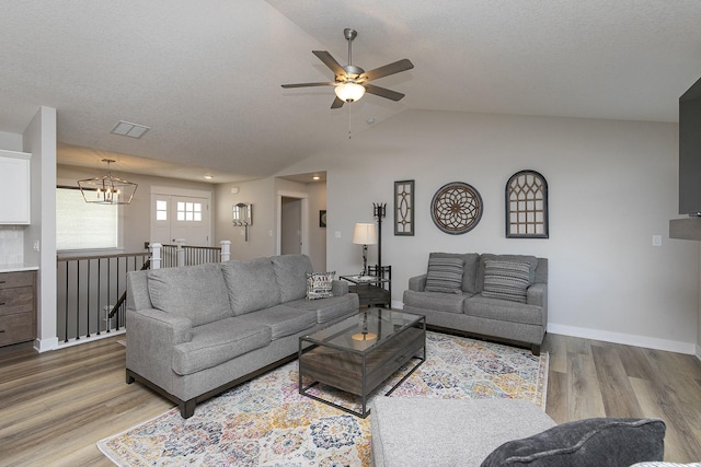 living room with vaulted ceiling, wood finished floors, visible vents, and baseboards