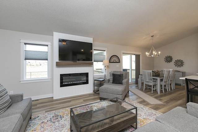 living room featuring a large fireplace, a textured ceiling, an inviting chandelier, and wood finished floors