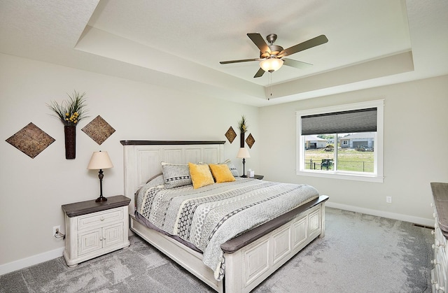 bedroom with a ceiling fan, a raised ceiling, light colored carpet, and baseboards