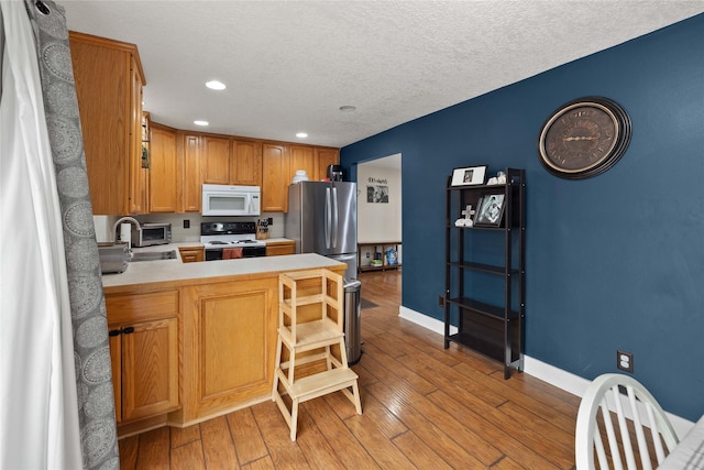 kitchen with electric range, white microwave, light wood-style flooring, a peninsula, and light countertops