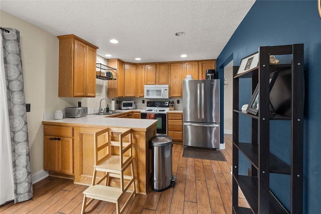 kitchen featuring electric stove, white microwave, freestanding refrigerator, a sink, and a peninsula